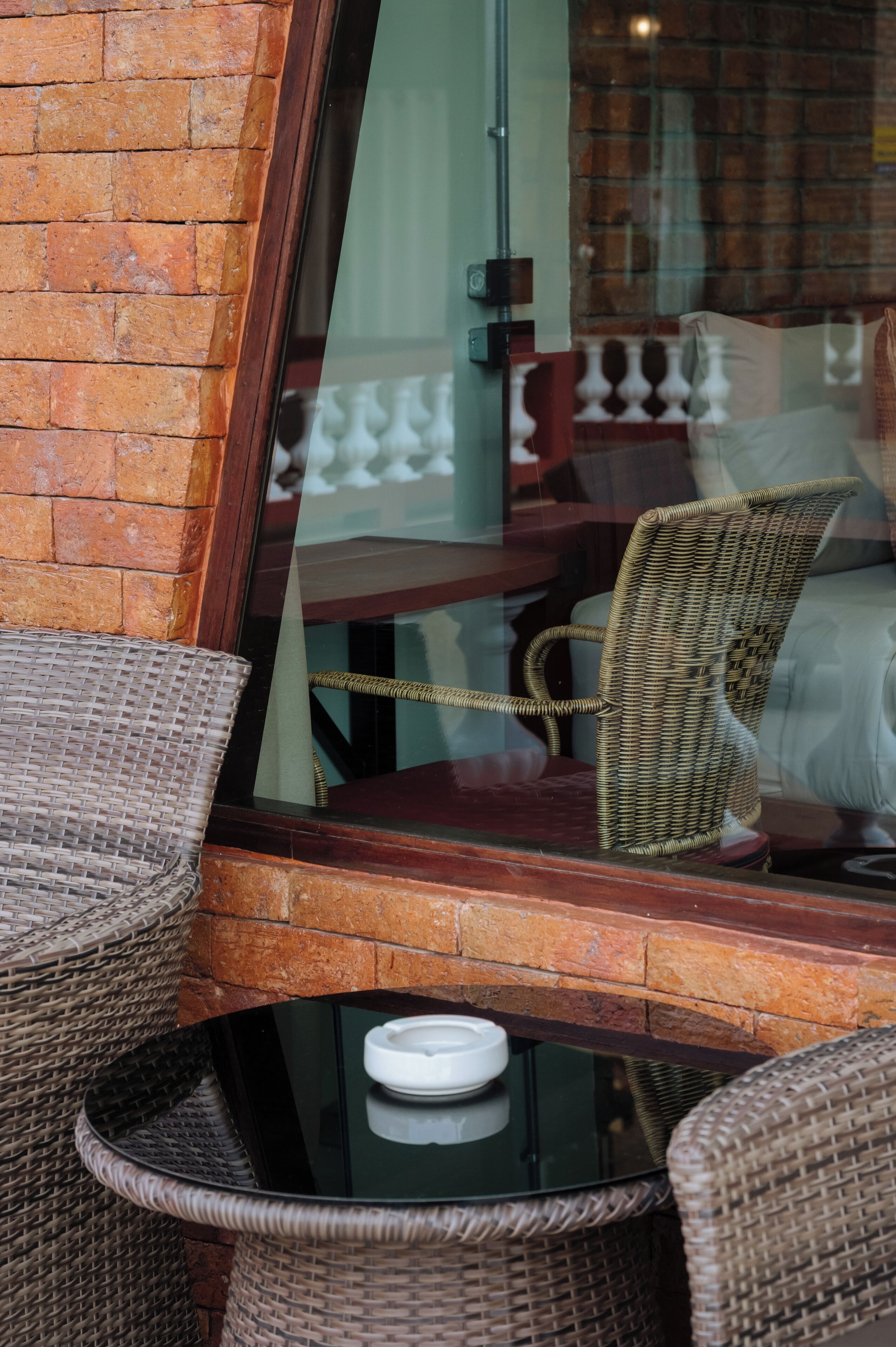 Wicker chairs and a glass table near a brick wall and window.