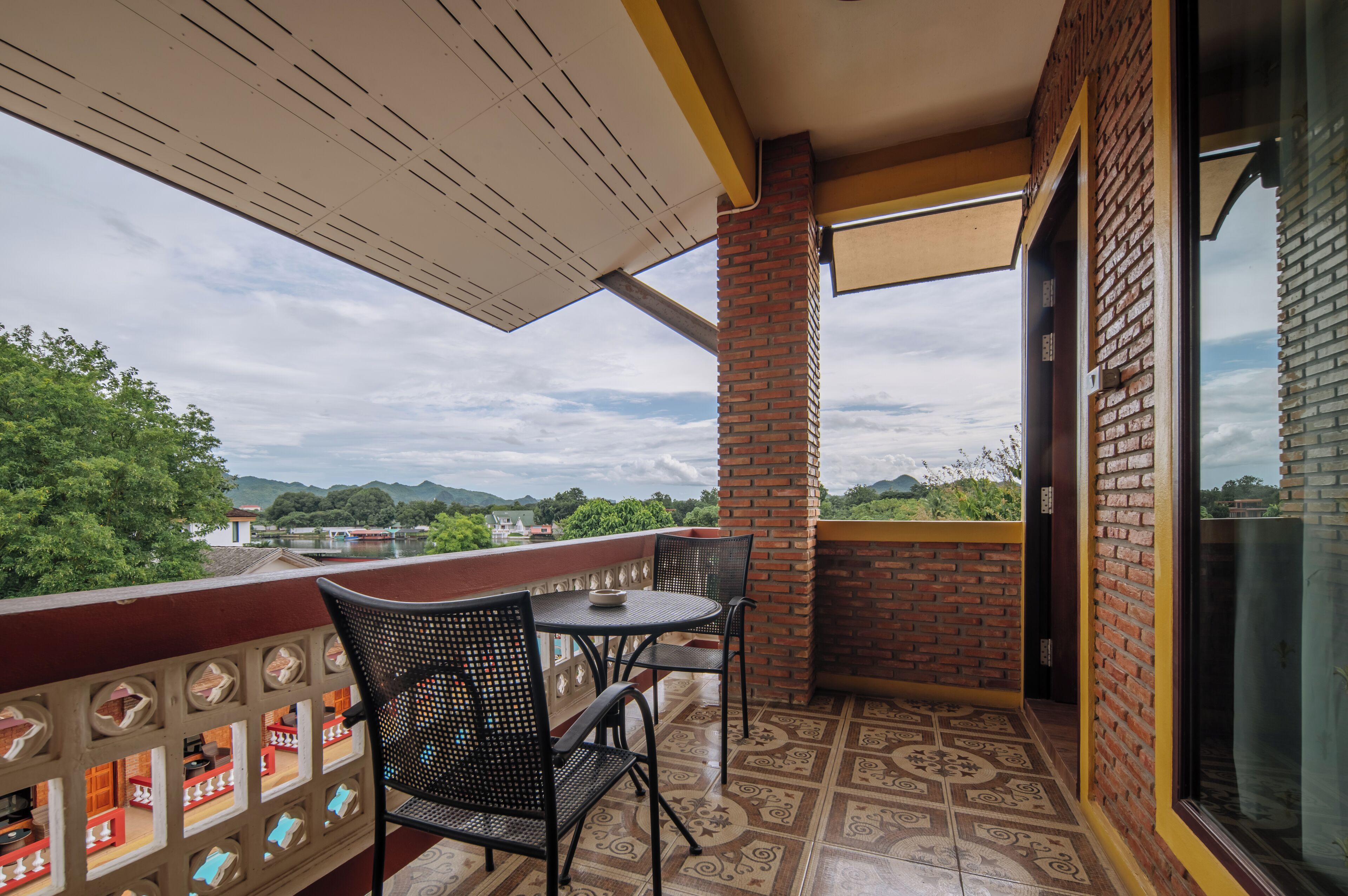 Uma varanda com mesa e cadeiras, um pilar de tijolos, e vista para um rio e montanhas.