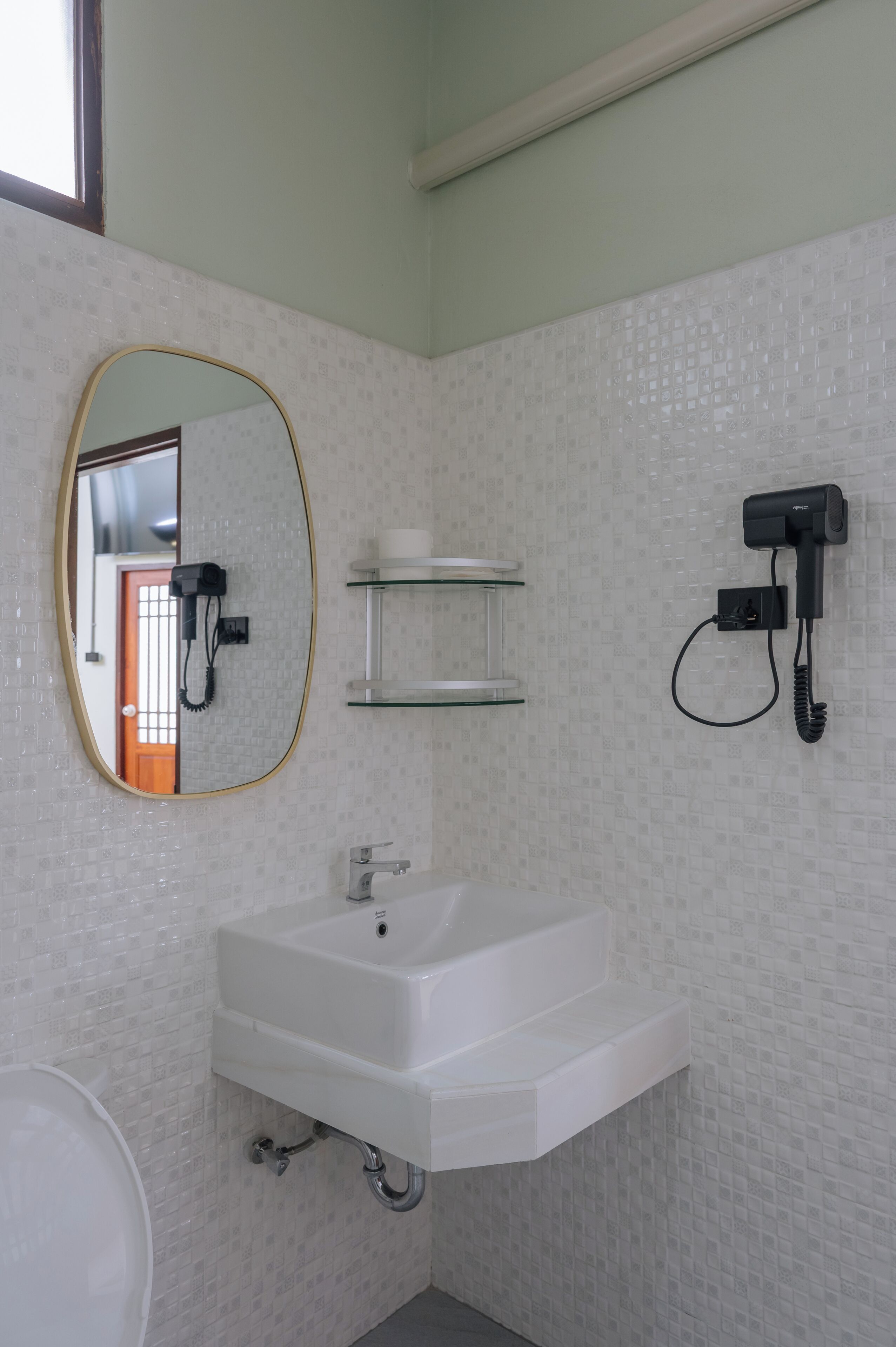 Een badkamer met een witte wastafel, een spiegel, een haardroger en een plankje.