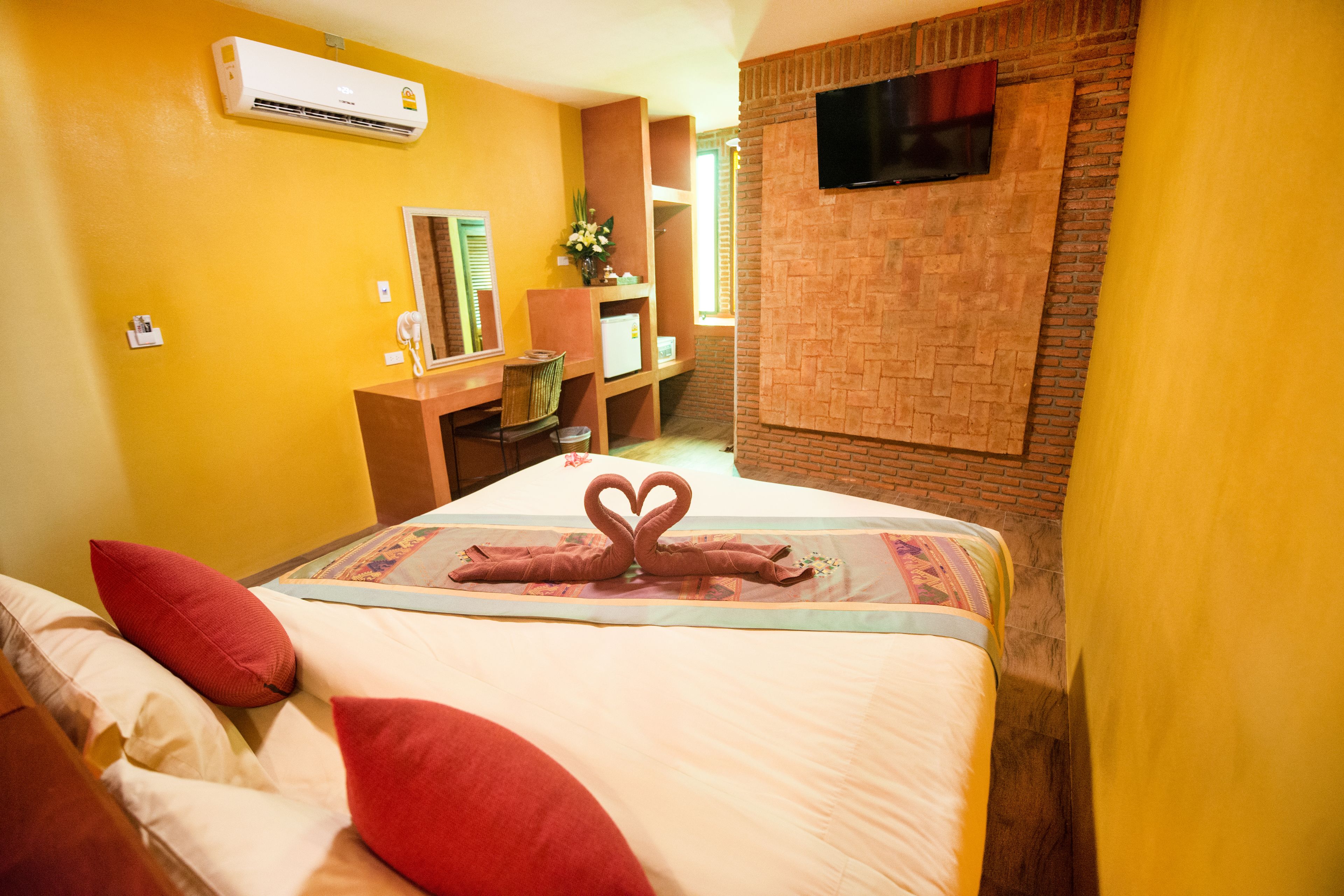 A hotel room with a bed, a desk, and a TV mounted on a brick wall.