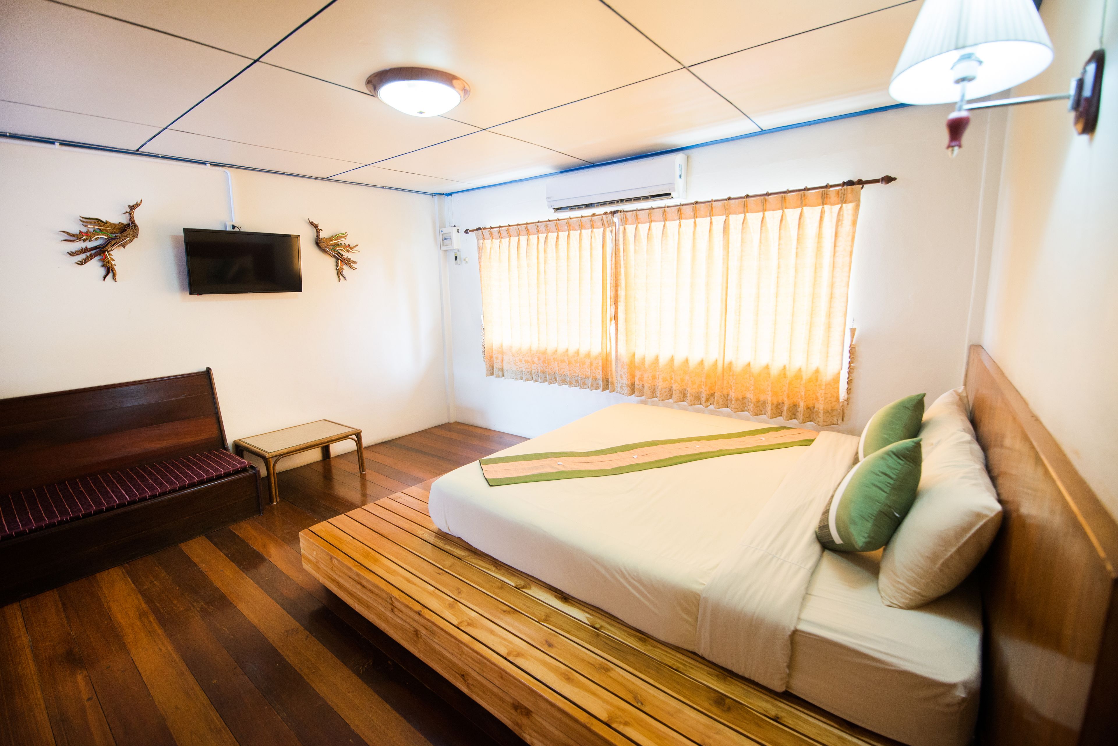 A bedroom with a bed, a bench, a TV, and curtains.