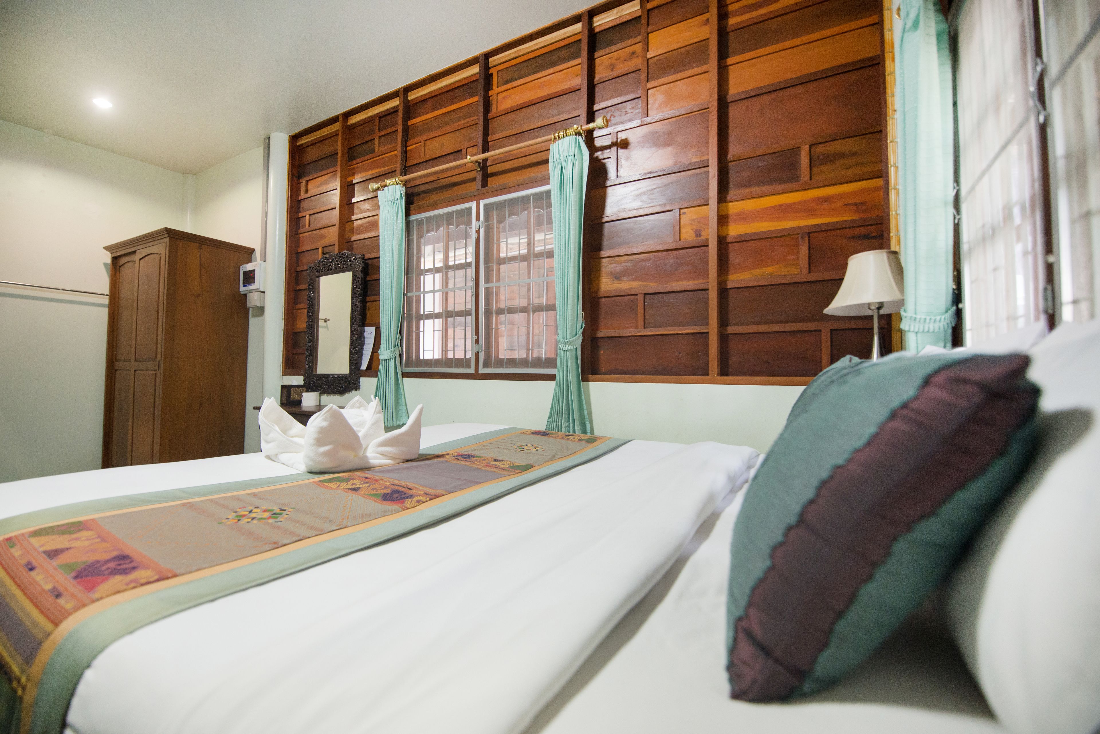 Une chambre d’hôtel avec une tête de lit en bois, un grand lit recouvert d’une couvre-lit décorative, une table de chevet avec une lampe et une armoire.