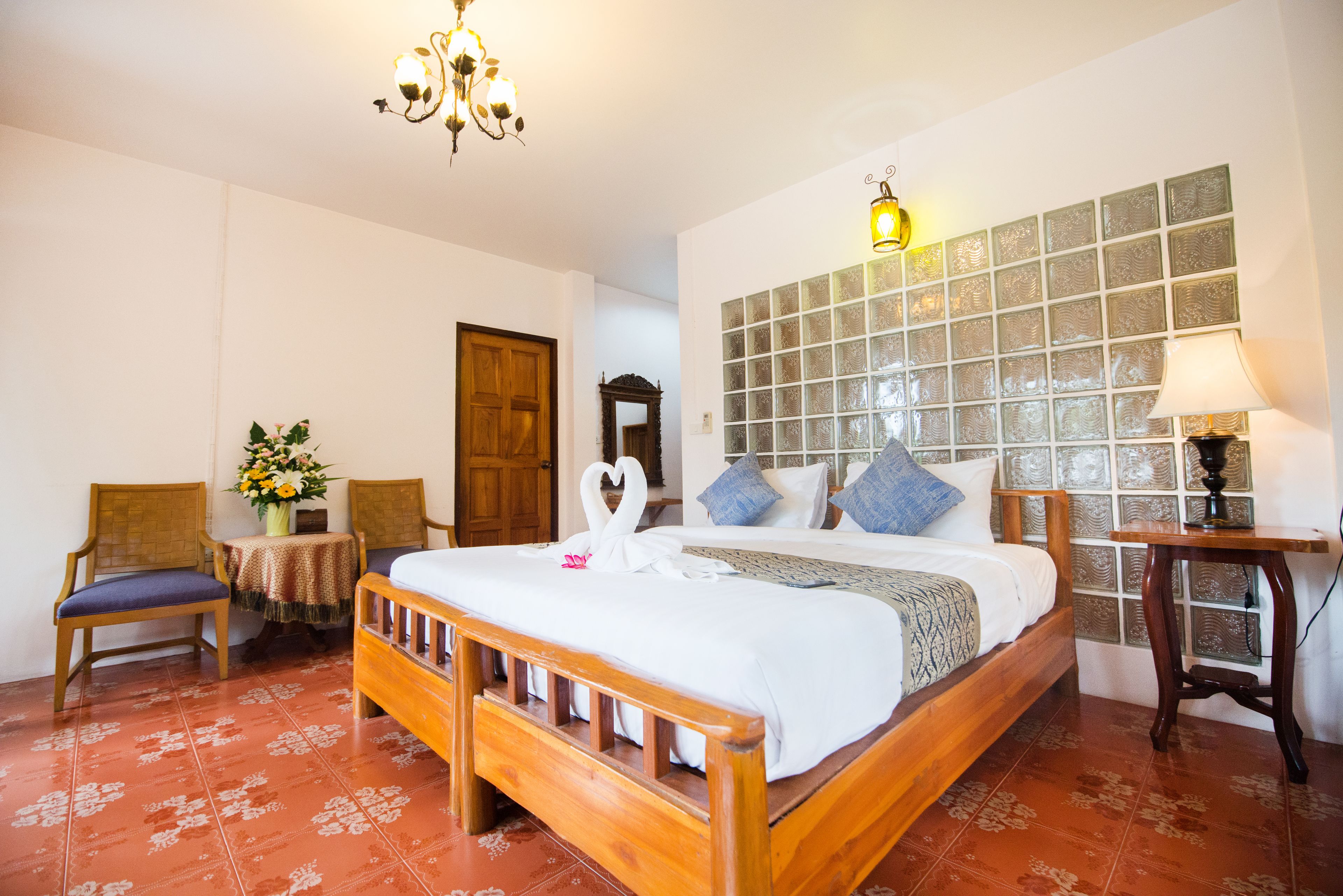 A hotel room with a wooden bed, a small table with a vase of flowers, a chair, and a chandelier.