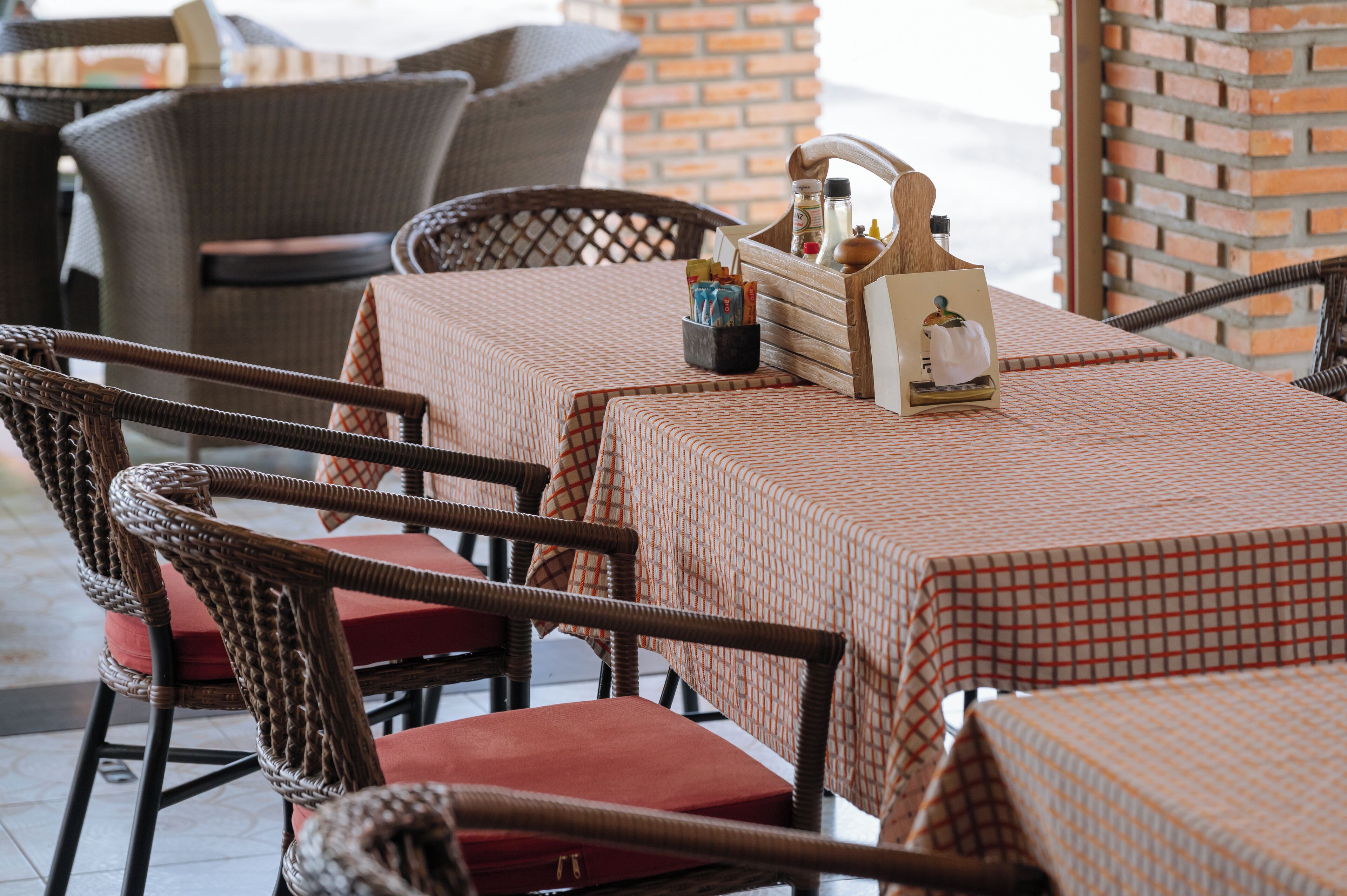 A patio area with wicker chairs and tables covered with patterned tablecloths.