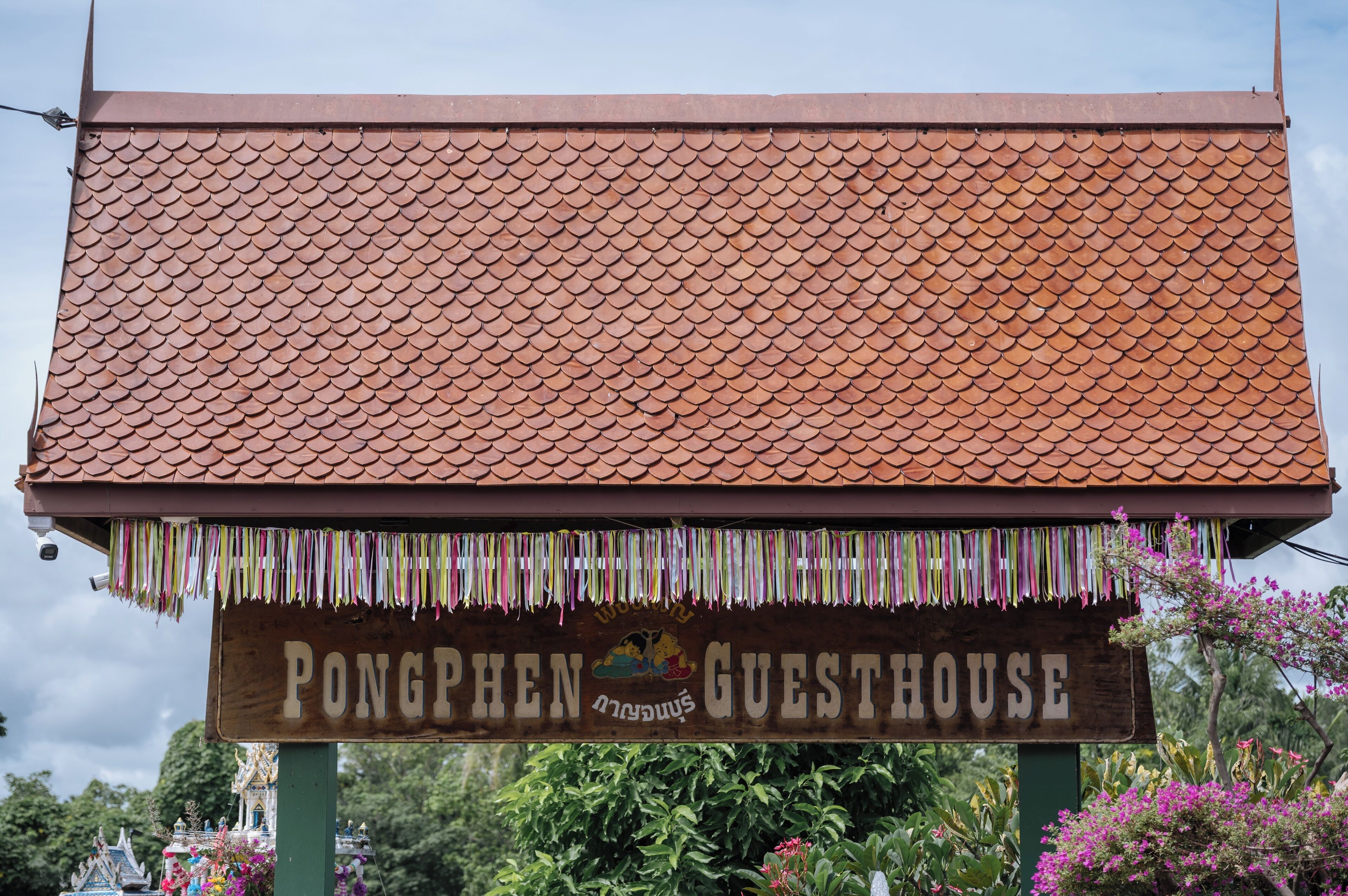 A sign for 'Pongphen Guesthouse' with a tiled roof and colorful hanging decorations.