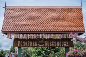 Un letrero que dice 'Pongphen Guesthouse', con techo de tejas y coloridas decoraciones colgantes.