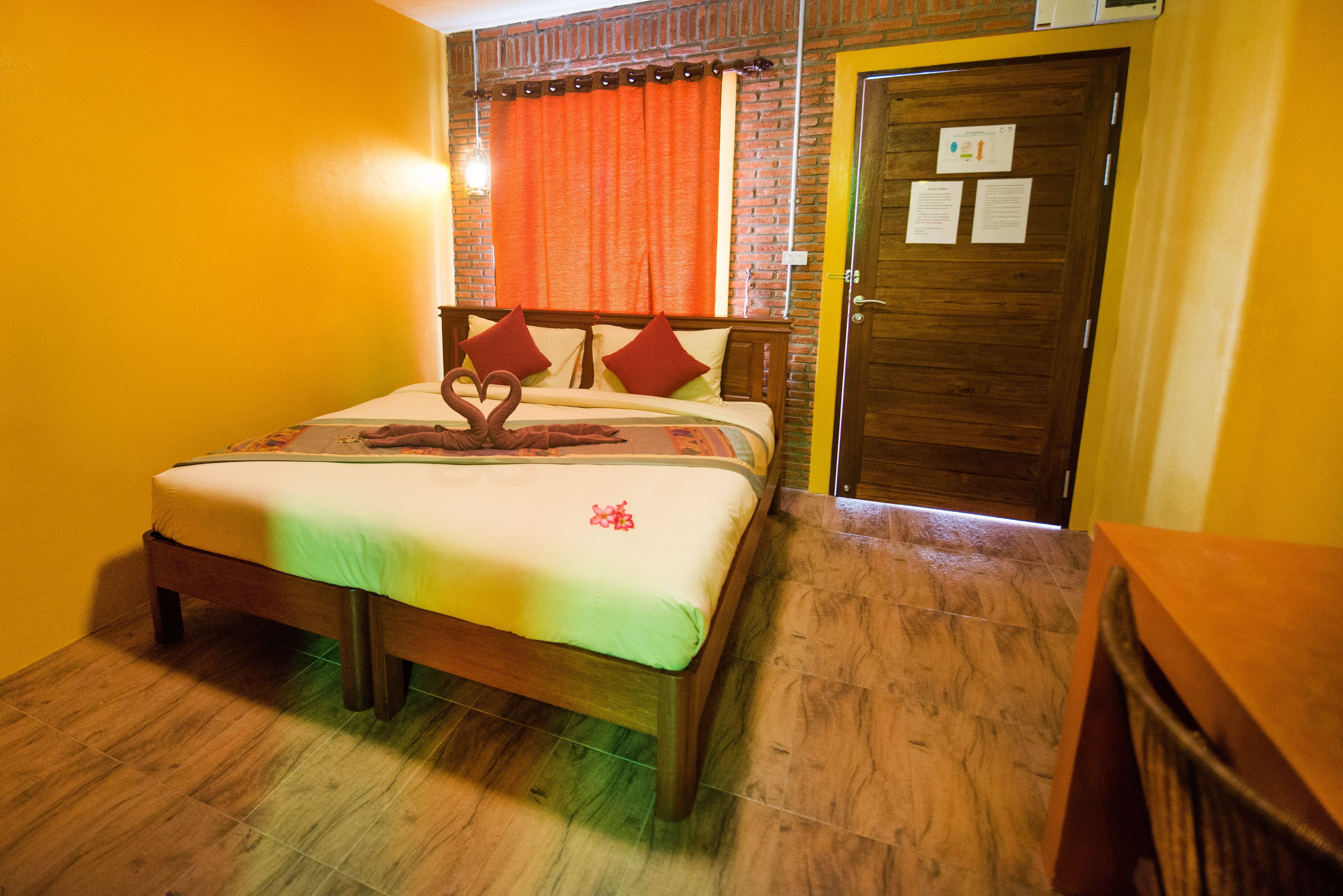 Habitación de hotel con cama de madera, cortinas naranjas, puerta de madera y suelo de baldosas.