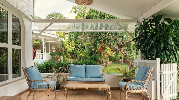 A covered patio with wicker furniture and a view of a lush garden. - Beau Vallon Bungalows (Mahé Island)