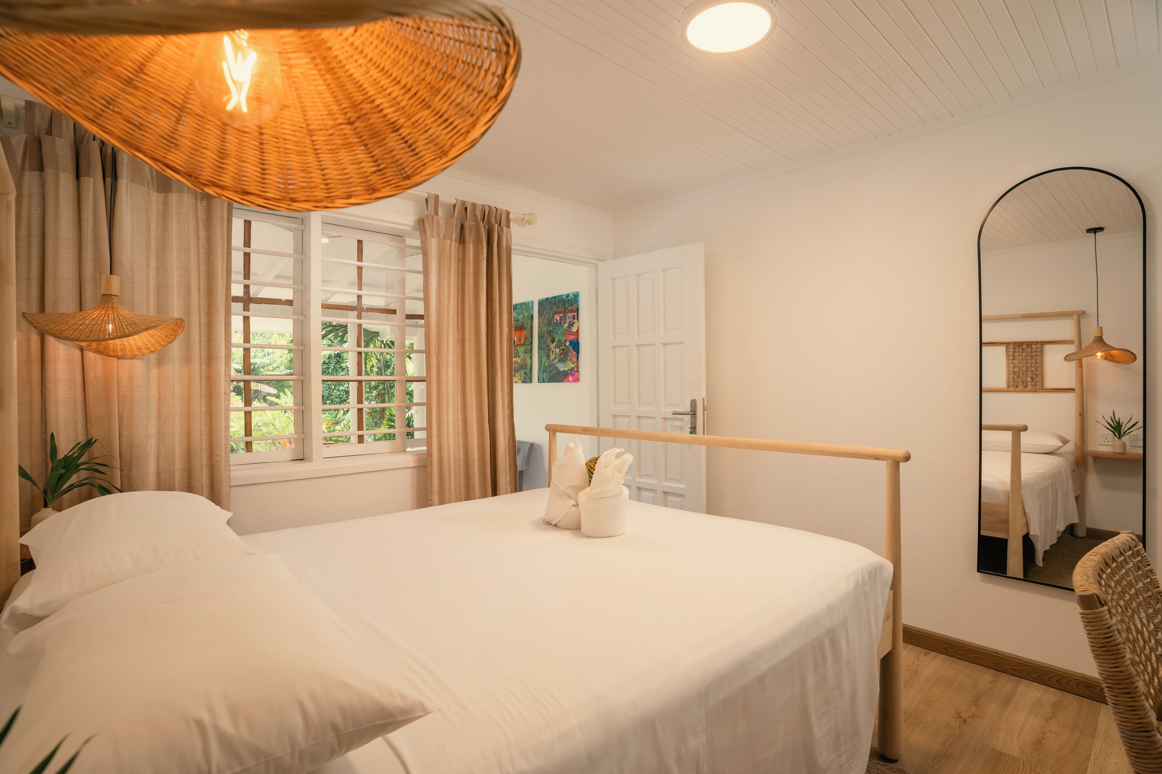 A neatly arranged bedroom with a large bed, a hanging light fixture, a mirror, and a window with curtains.