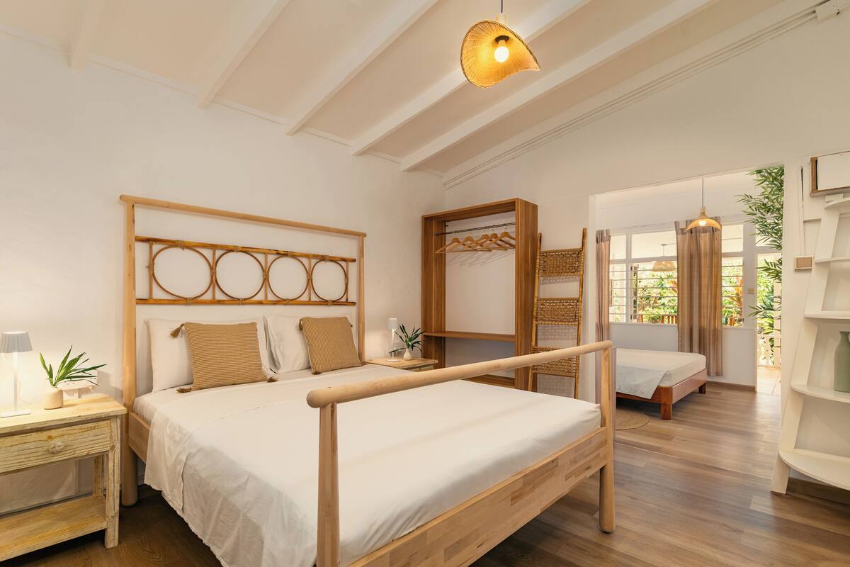 Ein Schlafzimmer mit einem hölzernen Bett, einem Nachttisch, einer Pendelleuchte und Blick ins Freie.