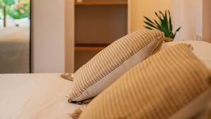 A bedroom with a bed, a hanging light fixture, a plant, and a mirror. - Beau Vallon Bungalows (Mahé Island)