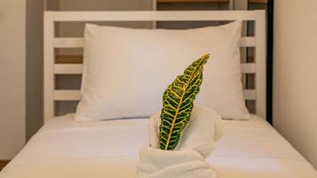 Een netjes opgemaakt bed met een wit kussen en een handdoek met een groen blad. Achtergrond is een witte kledingkast met een spiegel.