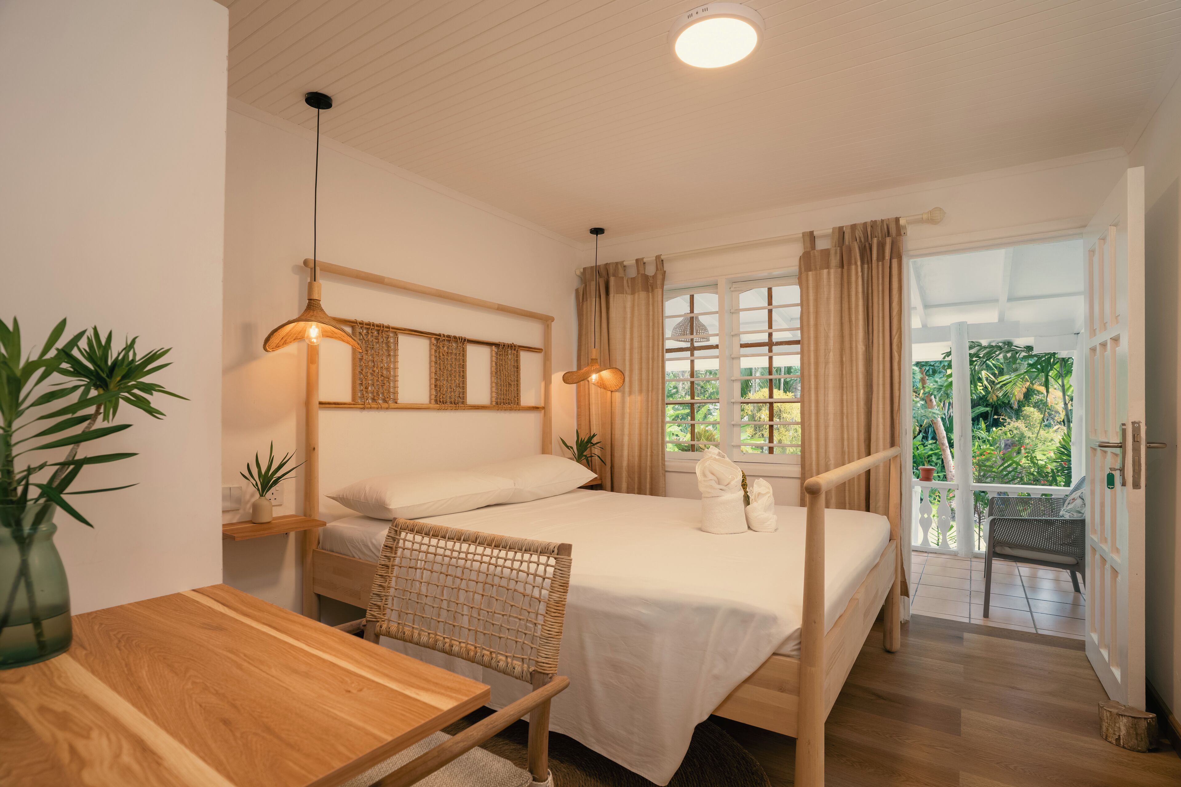 A bedroom with a bed, bedside table, chair, hanging light fixture, and a window with curtains.
