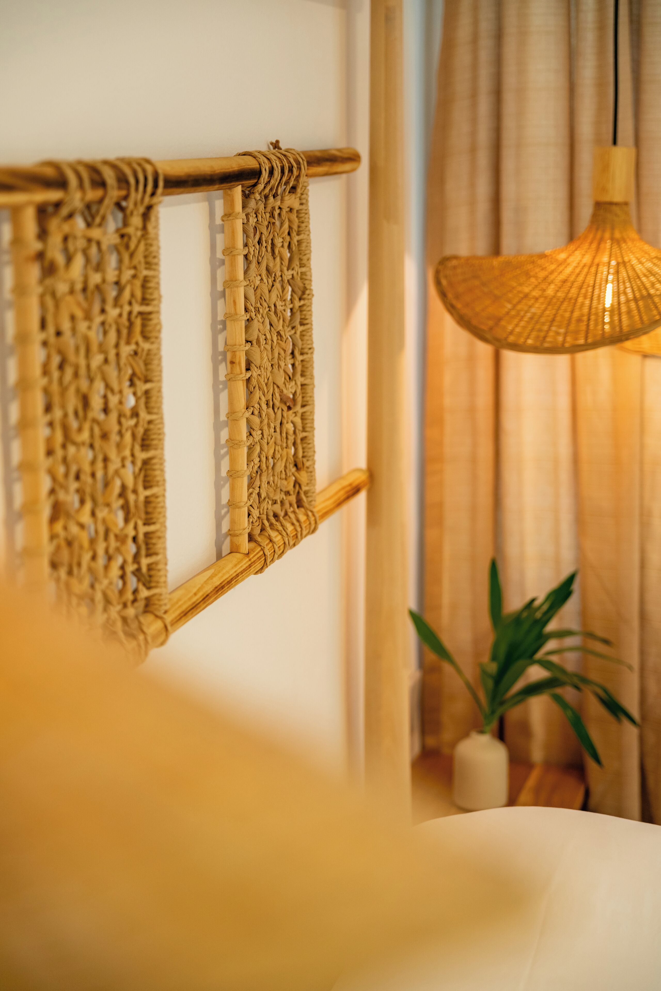 A room with a woven wall hanging, a hanging light fixture, and a potted plant.