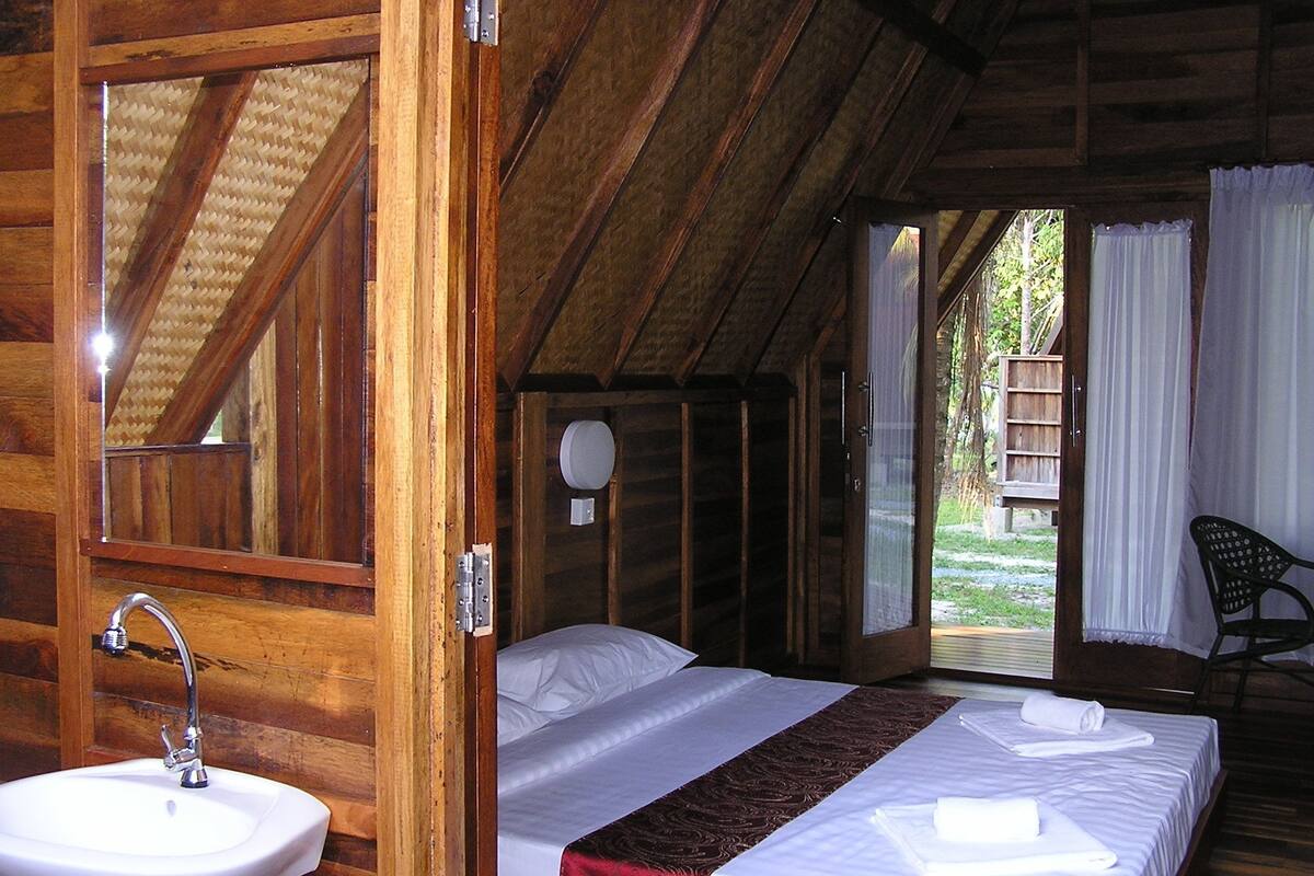 A wooden cabin bedroom with a bed, a sink, and a view of the outdoors.