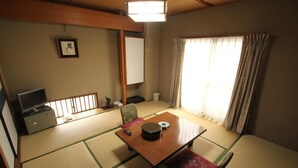 A traditional Japanese room with tatami flooring, a low table with a cushion, a television, and a sliding door. - Hotel Mimatsu (Nara)