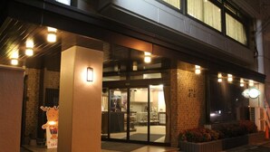 A hotel entrance with a glass door, a small outdoor seating area, and a cartoon character decoration. - Hotel Mimatsu (Nara)