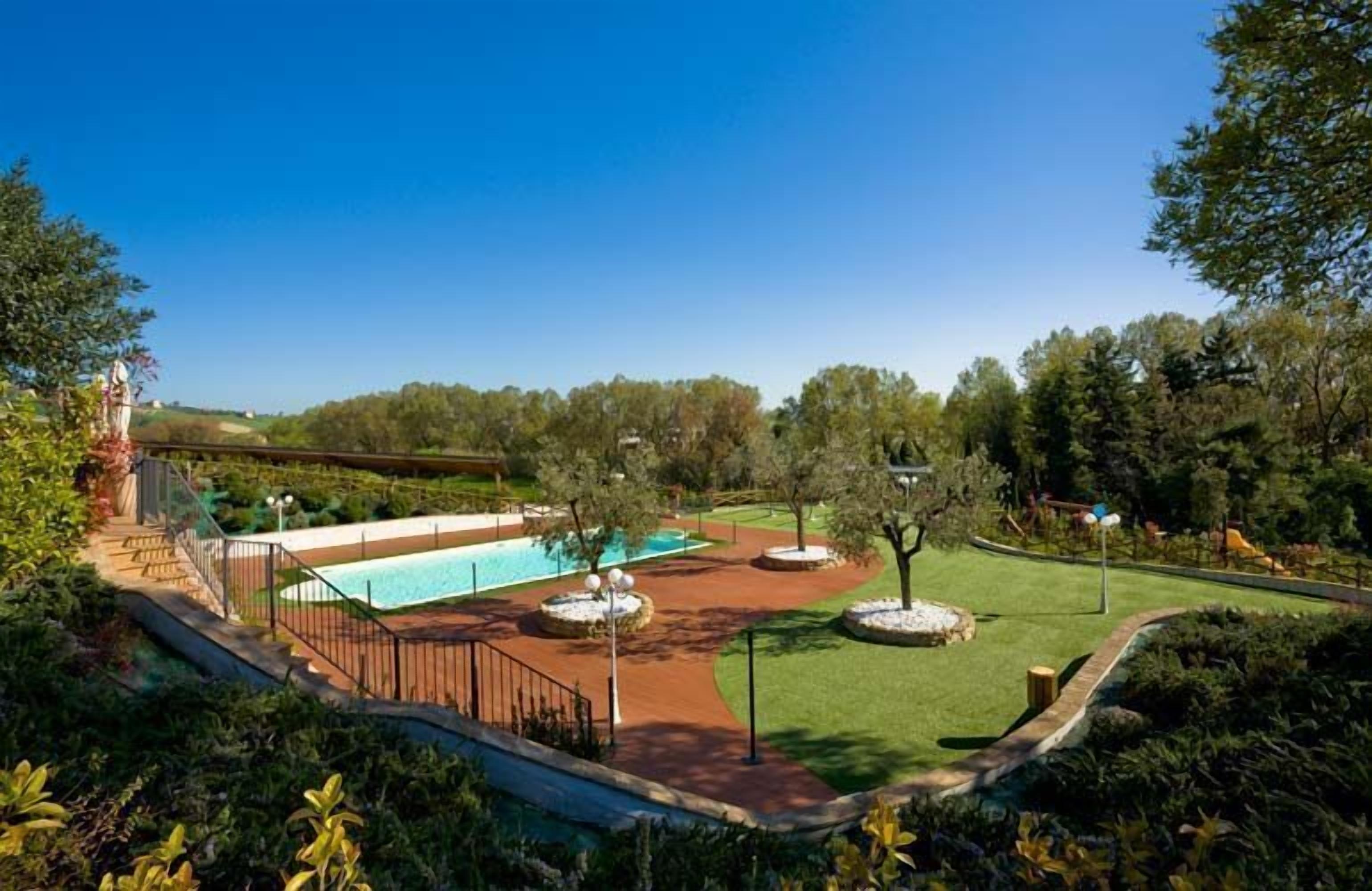 Un espacio exterior ajardinado con piscina, senderos y árboles.