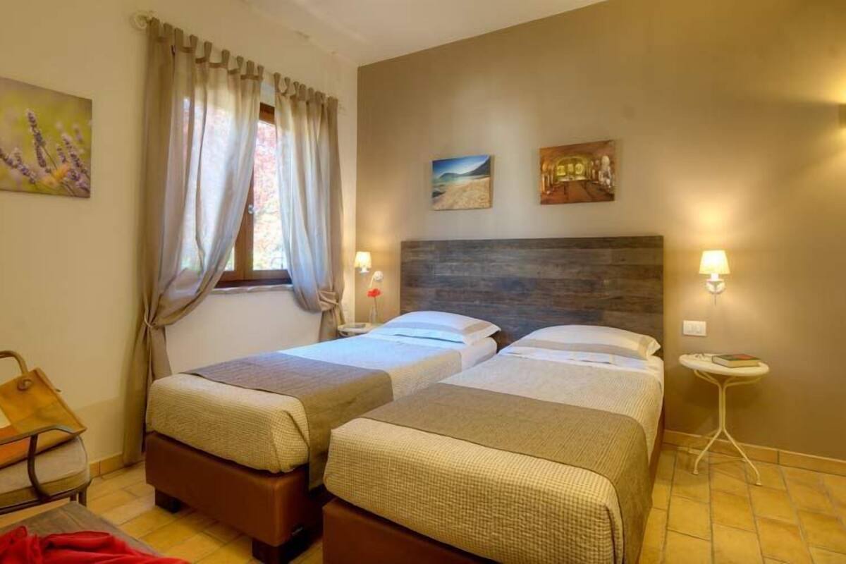Une chambre d’hôtel avec deux lits, une petite table, une chaise et des œuvres d’art accrochées aux murs.