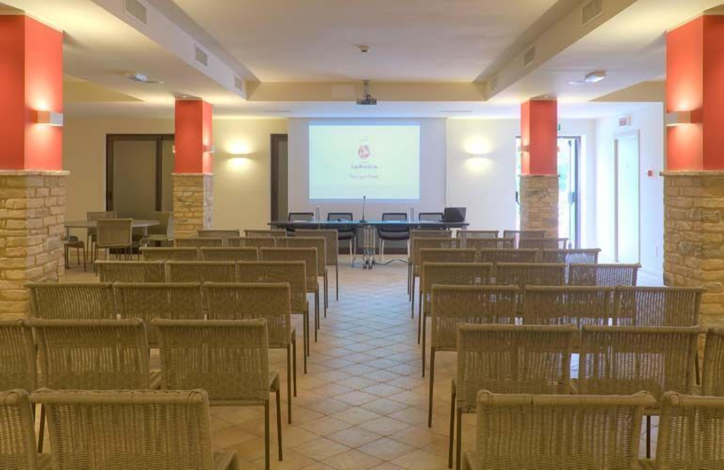 Un salón de conferencias con sillas de mimbre, una pantalla de proyector y un pilar de piedra.