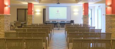 Un salón de conferencias con sillas de mimbre, una pantalla de proyector y un pilar de piedra.