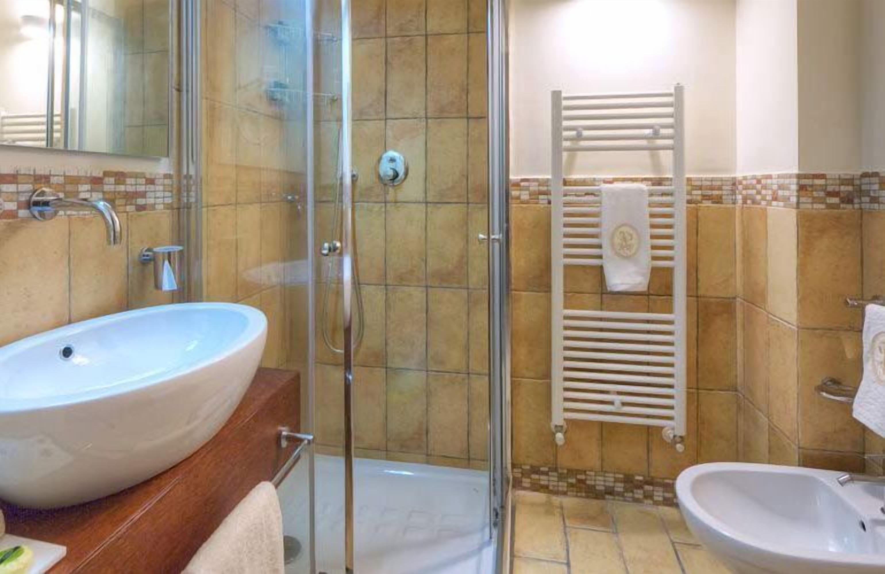Un baño con un lavamanos grande y blanco, una cabina de ducha con paredes de vidrio y un perchero blanco para toallas.