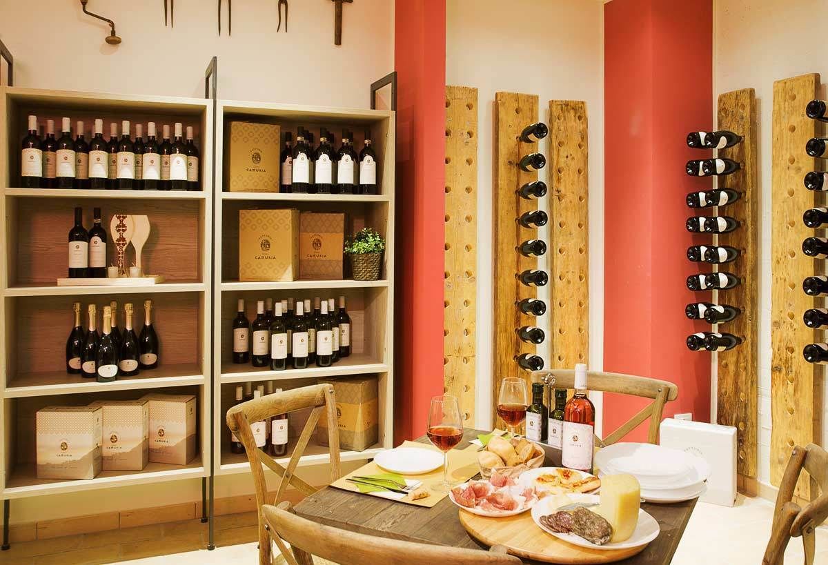 Zona pranzo con tavolo di legno apparecchiata per un pasto, circondata da scaffali e portabottiglie per vino.