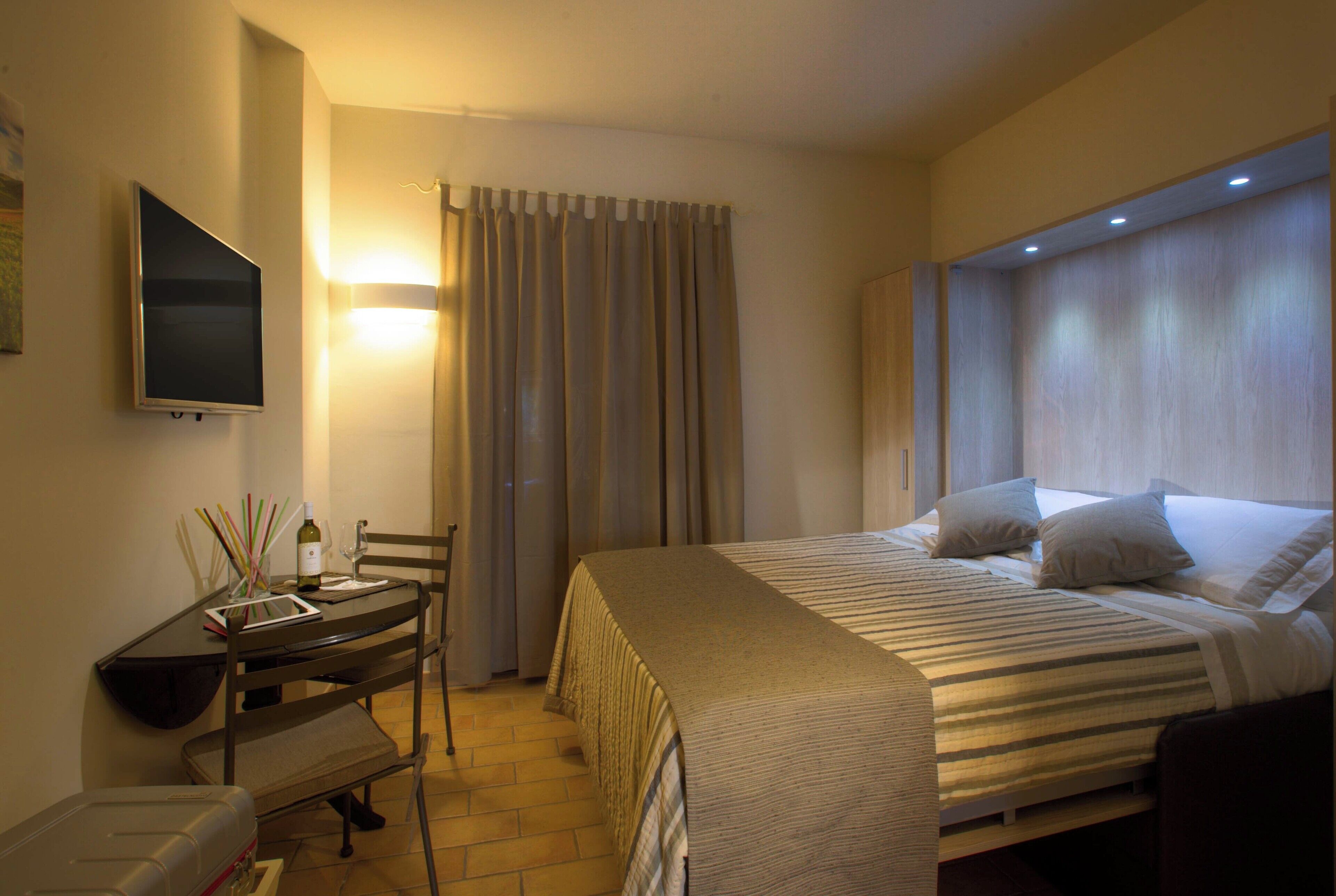A hotel room with a bed, a desk with a chair, a television, and curtains.