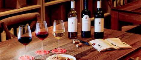 A wooden table with wine glasses, bottles, a corkscrew, a book, and a plate of pastries.