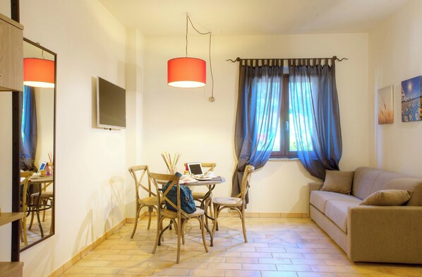 Una habitación con una mesa de comedor, sillas, un sofá, un televisor y una ventana con cortinas.