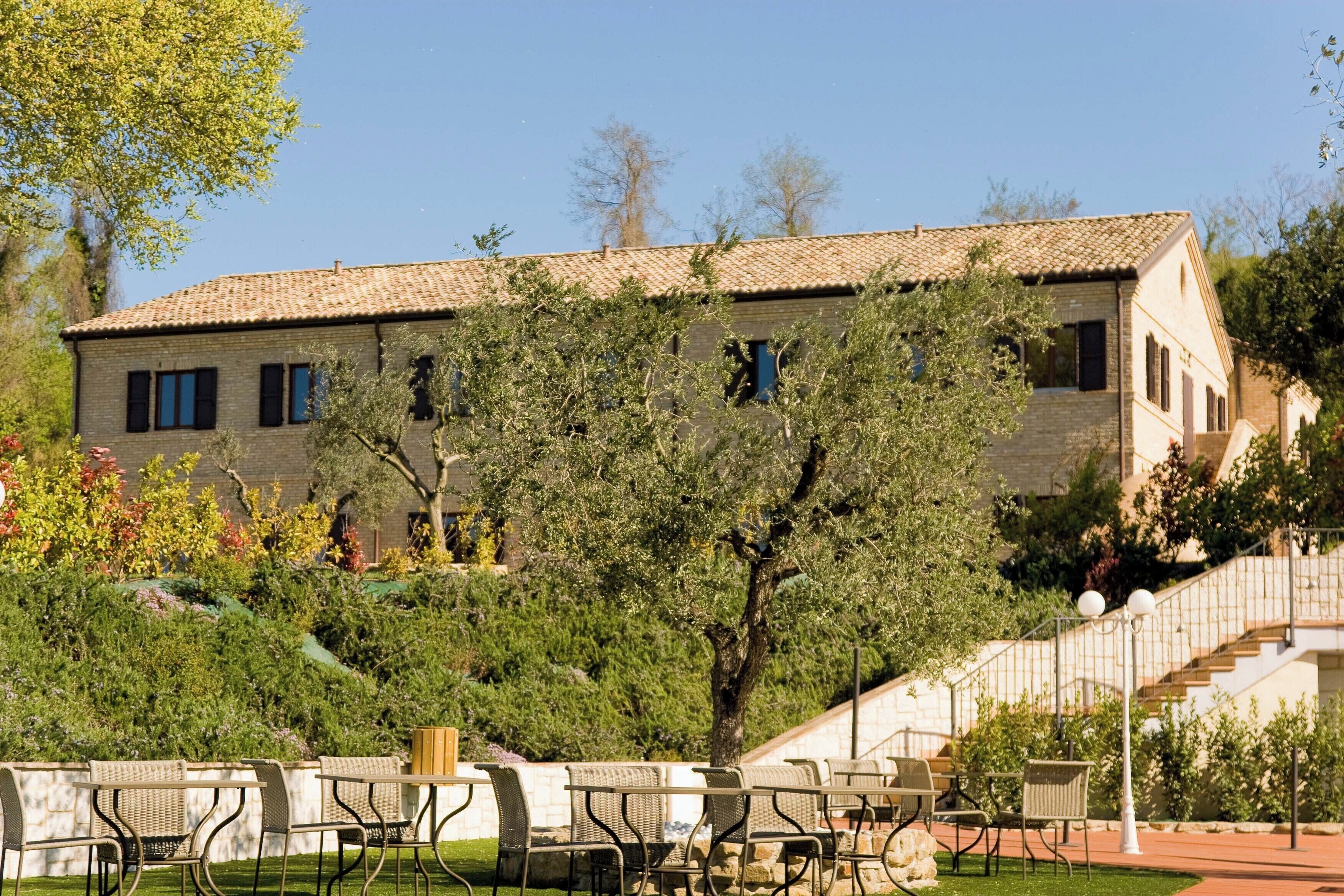 A building with a tiled roof, surrounded by greenery and outdoor seating.