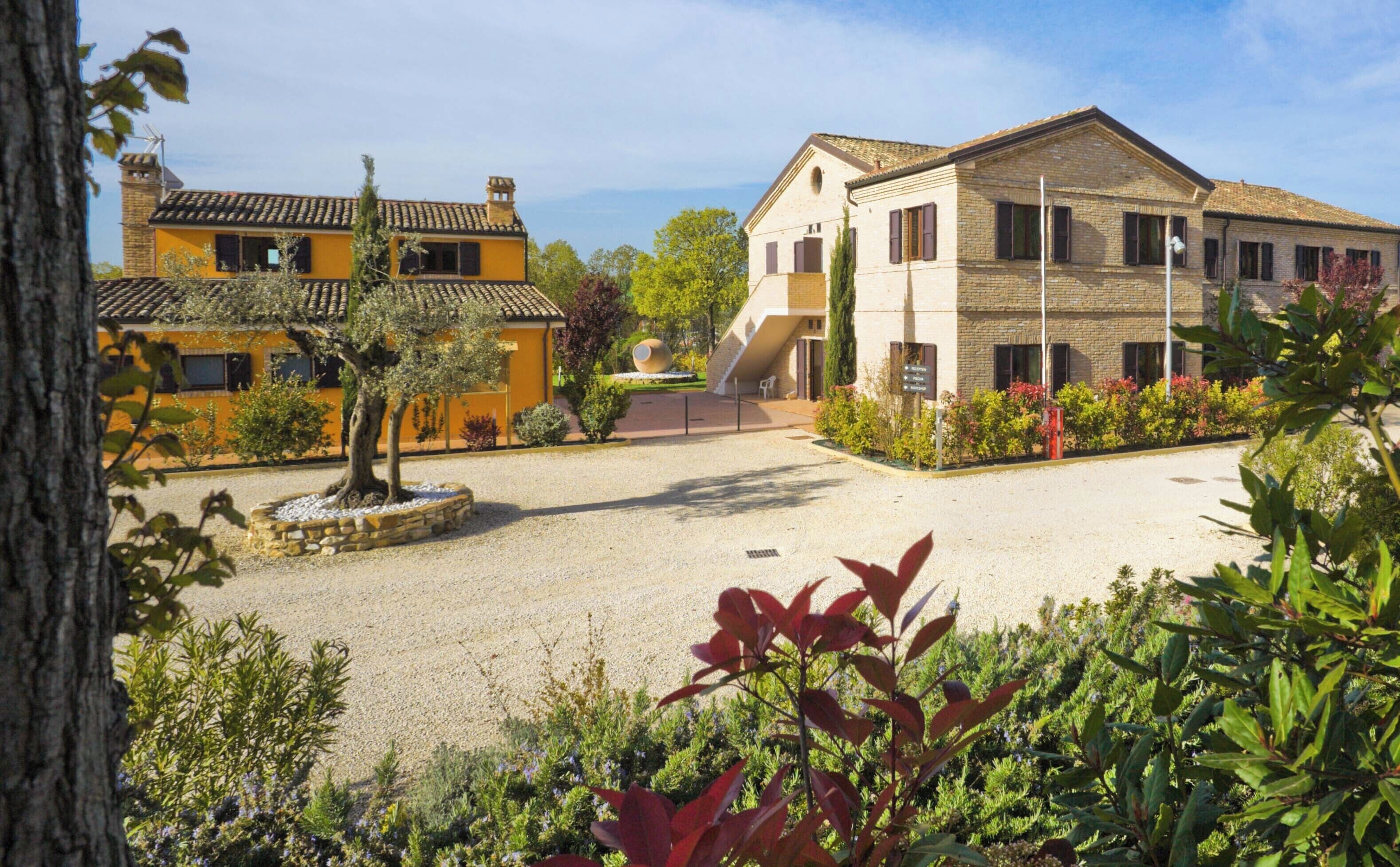 A courtyard with a yellow building, a stone wall, and a tree.