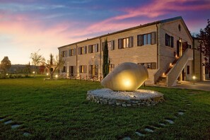 A modern building with a large spherical sculpture in the foreground, surrounded by a well-maintained lawn. - Villa Gens Camuria (Camerano)