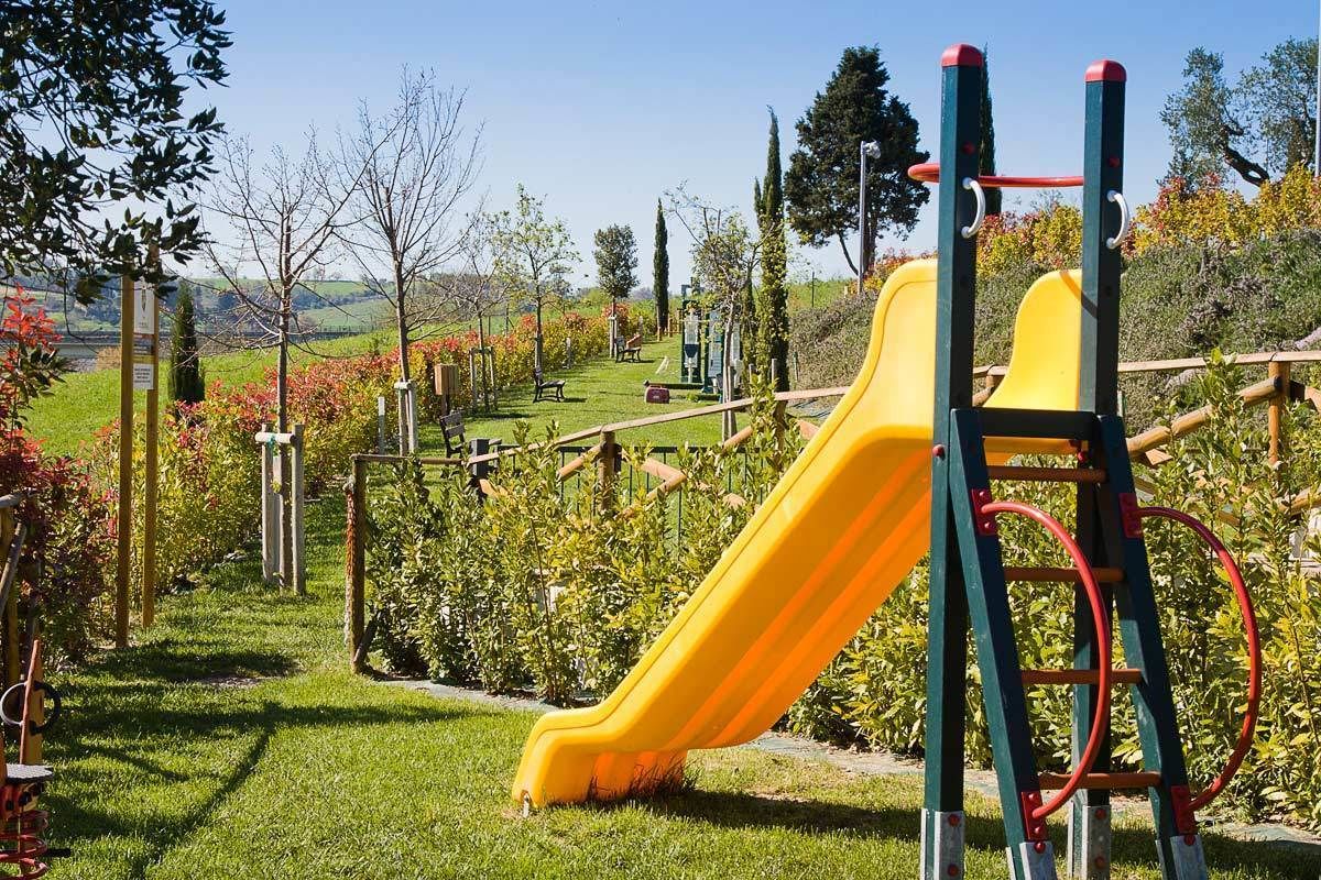 Un terrain de jeux avec un toboggan jaune et des structures d’escalade, le tout aménagé dans un jardin paysager.