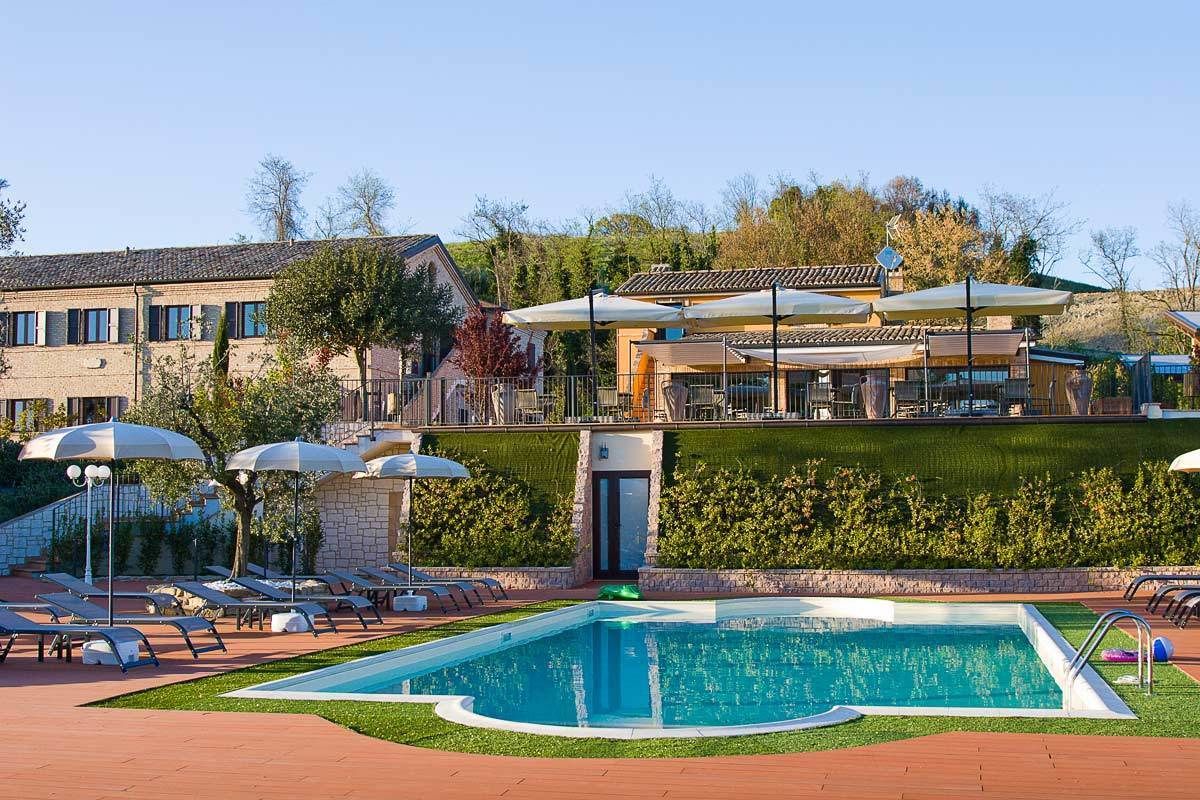 Une piscine entourée de chaises longues et de parasols, elle-même bordée d’un jardin aménagé et d’un bâtiment doté d’un toit en tuiles.