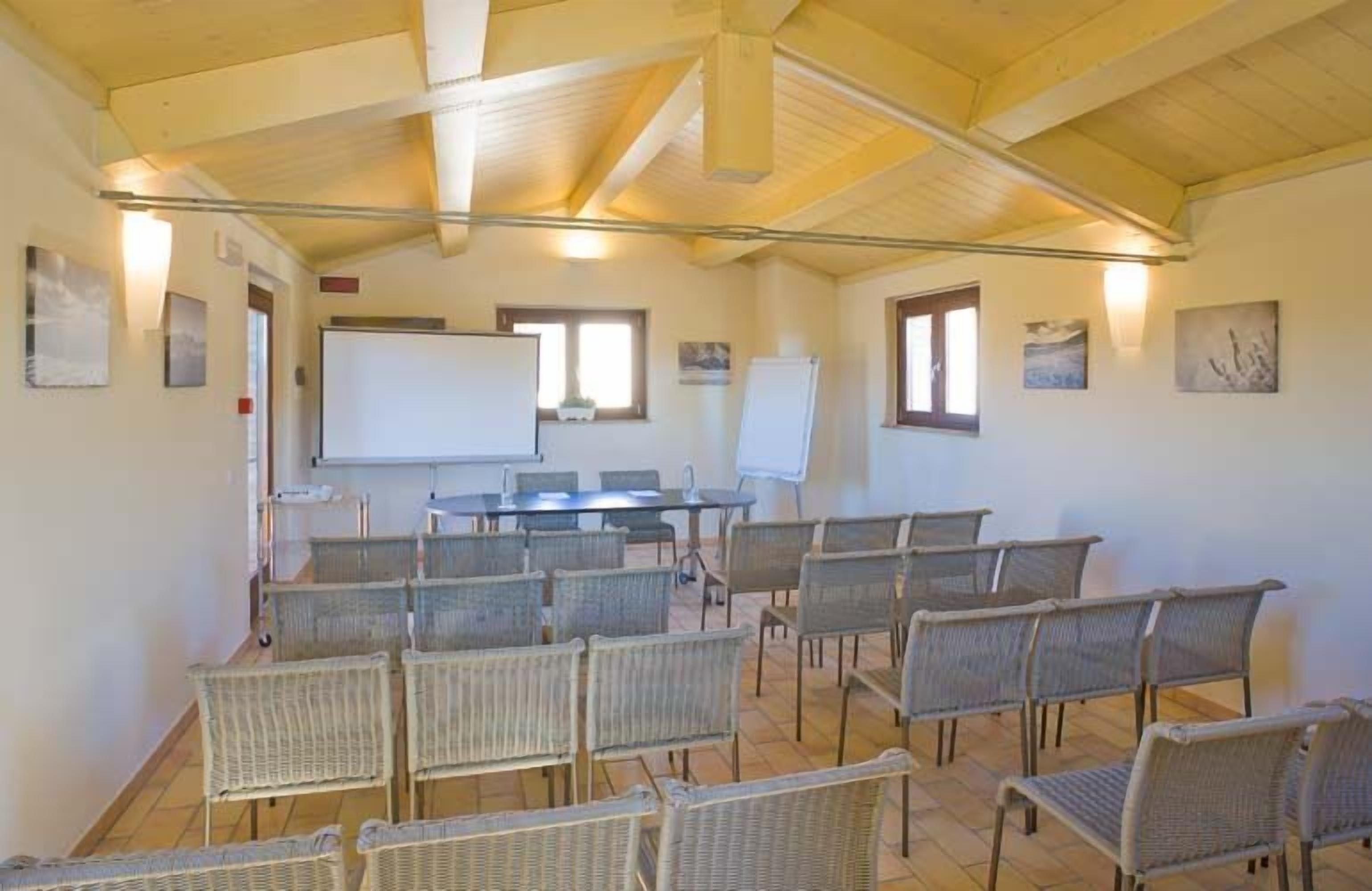 Une salle de conférence avec une longue table, plusieurs chaises en osier, un tableau blanc et des tableaux encadrés accrochés aux murs.
