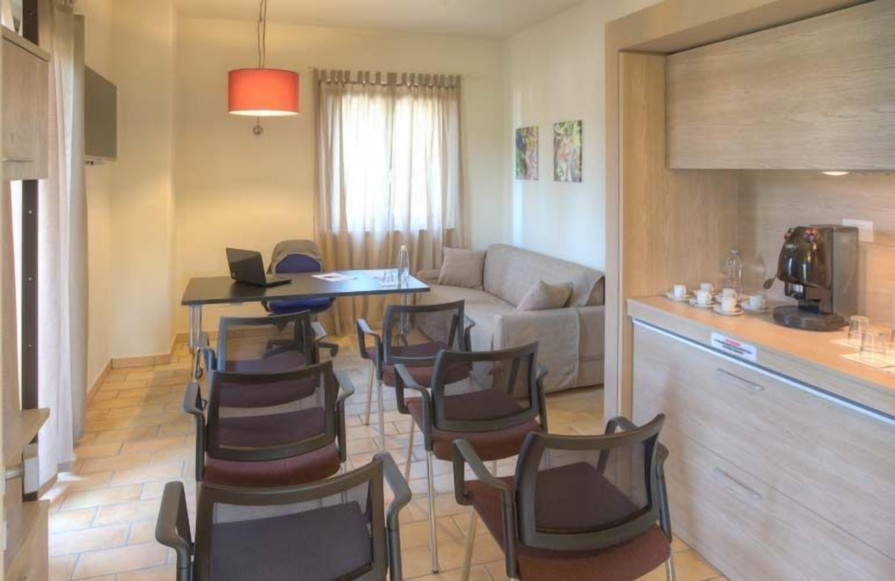 A modern living room with a sofa, a dining table with chairs, a coffee machine, and a TV.