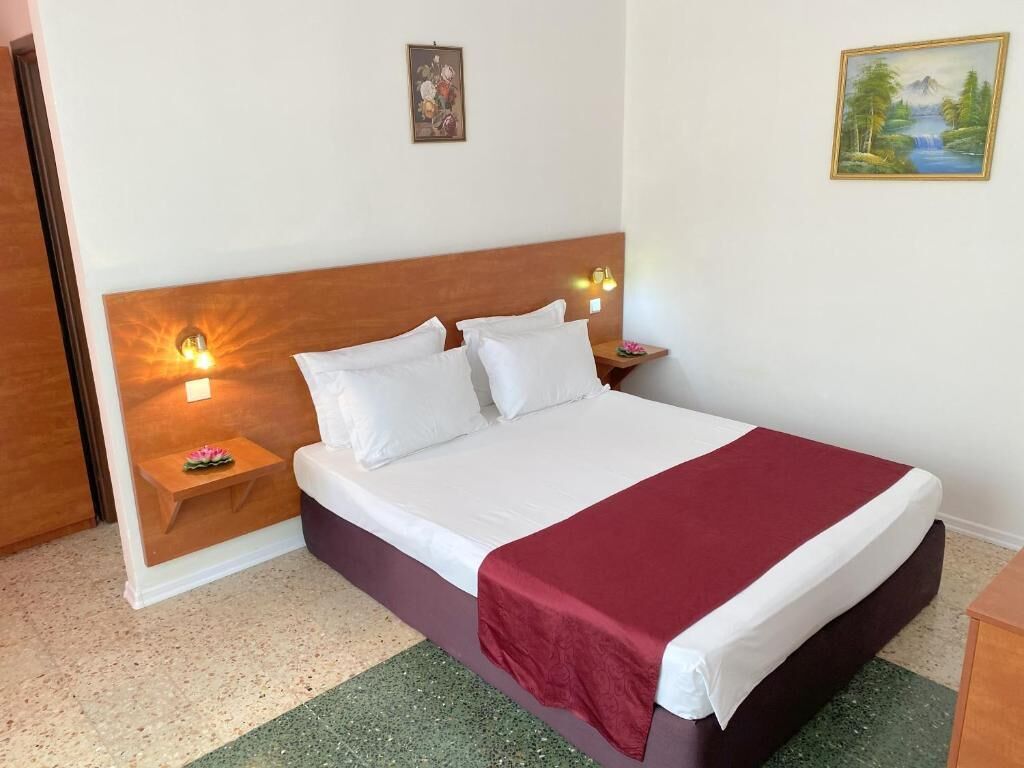 A neatly made bed with white linens and a red blanket, a wooden headboard, bedside lamps, and a small table with a flower.