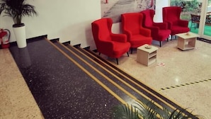 A lobby with a black and beige floor, red chairs, a large painting, and a plant. - Tomis Hotel Neptun  (Neptun)