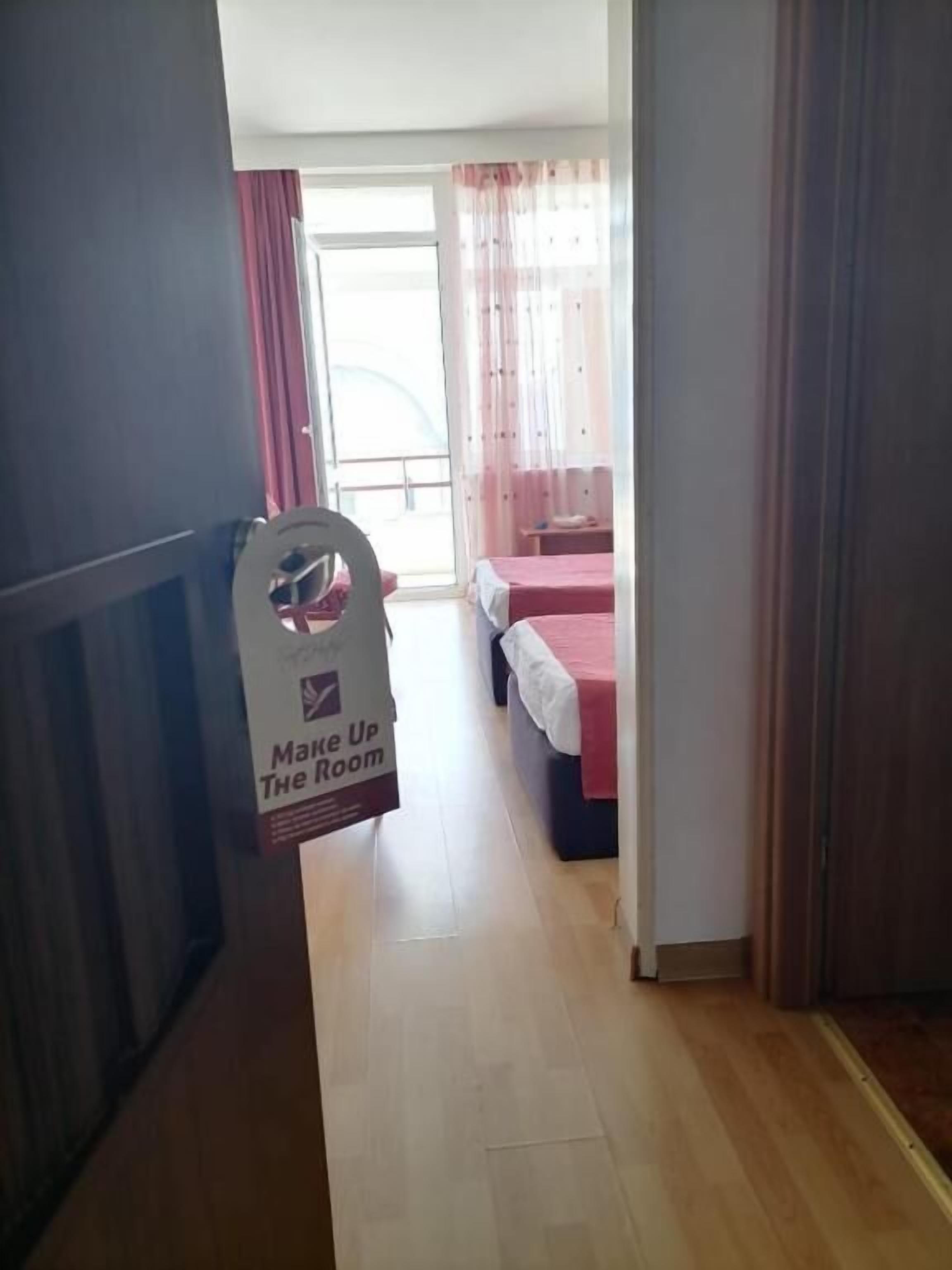 A hotel room with a bed, a small table, and a window with curtains. There is a sign that says "Make Up The Room".