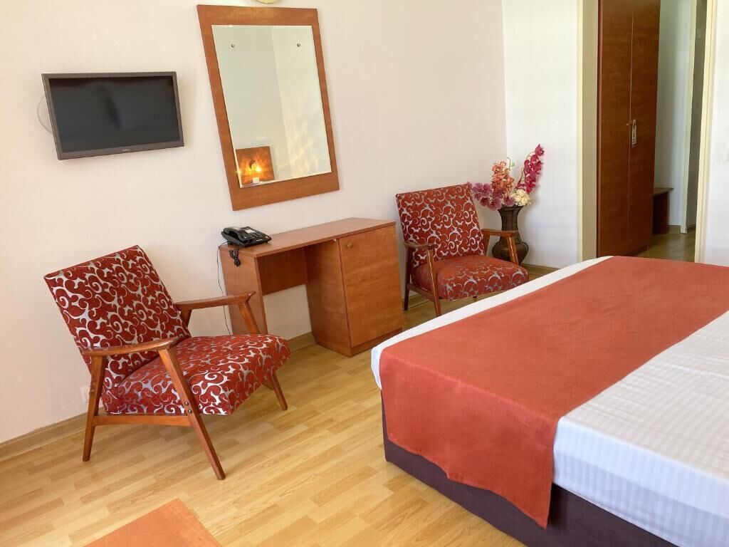Ein Hotelzimmer mit einem Bett, zwei gemusterten Stühlen, einem Schreibtisch, einem Spiegel und einem Fernseher.
