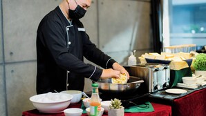 A chef preparing food in a kitchen with a red tablecloth, a toaster, and various bowls and bottles. - Sun City Suites (General Santos)