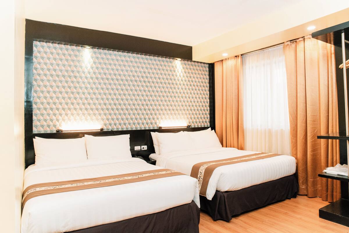 A hotel room with two beds, a large window with curtains, and a wall-mounted TV.