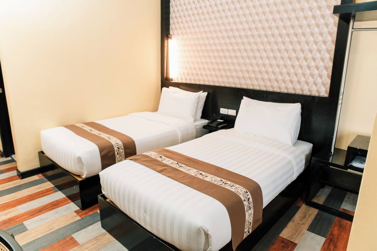 Two single beds with white and brown bedding, a patterned wall headboard, and a striped carpet.