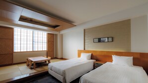 Ein Hotelzimmer mit zwei Betten, einem Holzkopfende, einem kleinen Tisch und einem großen Fenster.