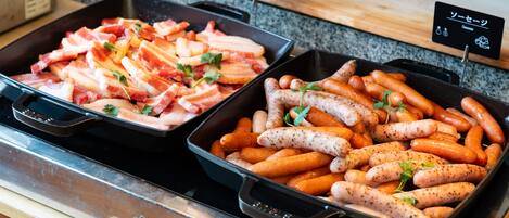 Dos sartenes de comida, una con tocino y la otra con salchichas, sobre una encimera.