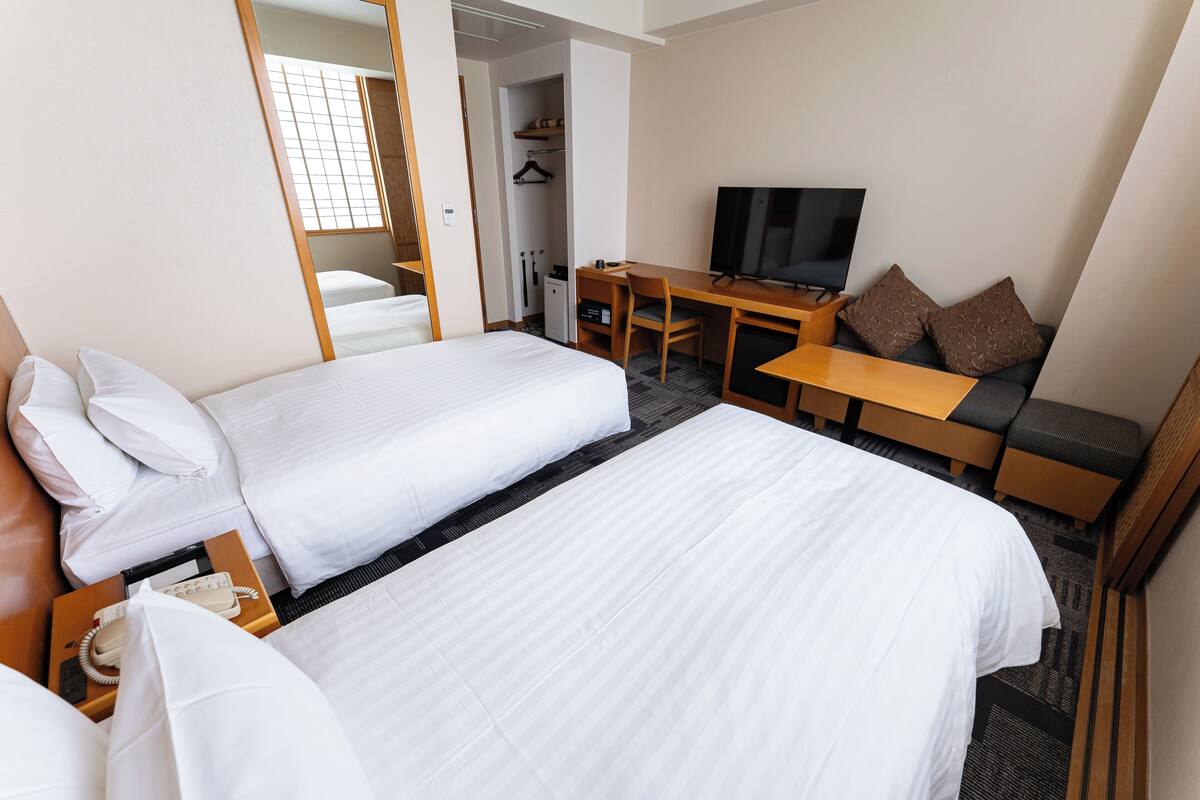 Ein Hotelzimmer mit einem großen Bett, einem Schreibtisch mit Stuhl, einem Fernseher und einem Sofa mit Kissen.