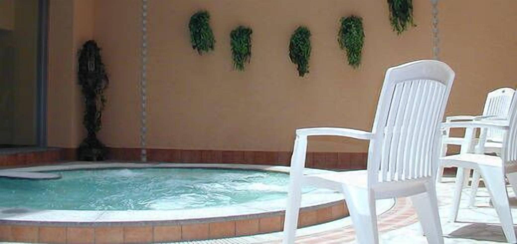 A hot tub area with a pool, white chairs, and green wall decorations.