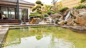 Ein friedlicher Innenbereich mit einem Teich mit Koi-Karpfen, Felsformationen und einem kleinen Wasserfall.