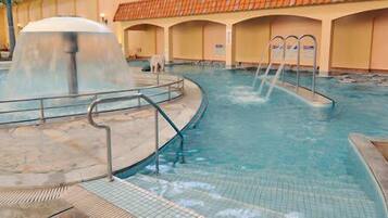 An indoor swimming pool with multiple lanes, a water fountain, and a seating area with a tiled floor.